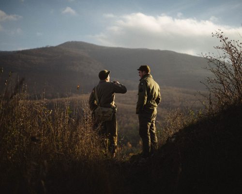 Two men dressed in coveralls talking with mountain in background